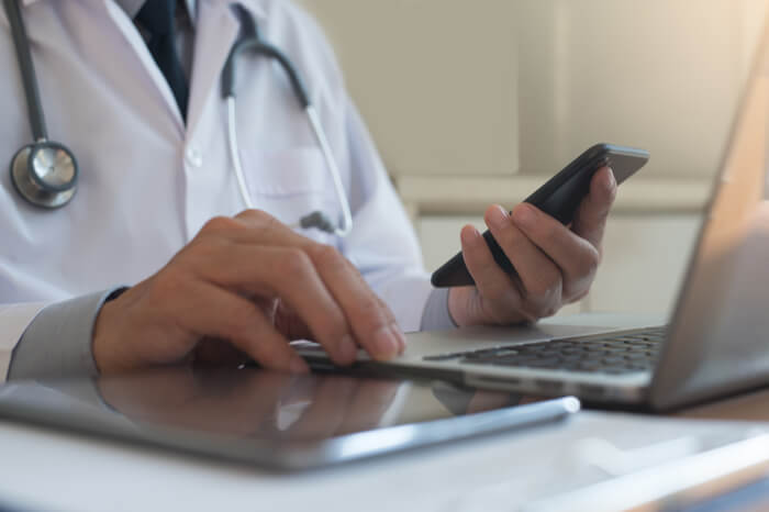 Arzt mit einem Mobiltelefon vor einem Laptop